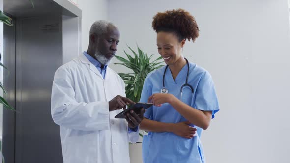 Diverse female and male doctors standing in hospital discussing over tablet