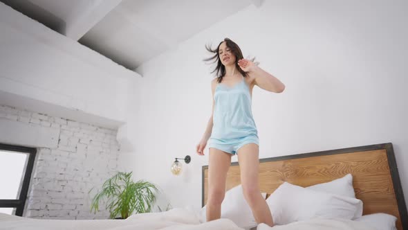 Happy Young Slim Woman Jumping on Bed in Slow Motion and Falling Down Smiling