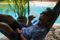 Man resting in a hammock and vaping and letting off steam from an electronic cigarette - PhotoDune Item for Sale