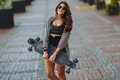 Beautiful young woman with longboard on the bridge in the city in sunny weather. Young hipster girl - PhotoDune Item for Sale