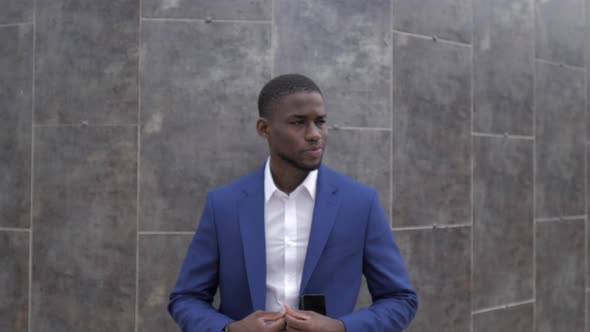 Businessman with smartphone in front of grey wall