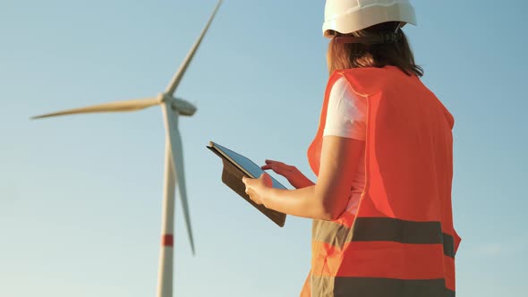 Female an Engineer in a Helmet and an Orange Vest Controls the Operation of a Wind Turbine Using a