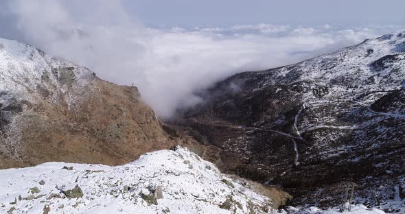 Aerial Flying Moving Forward Over Snowy Mountain Ridge Valley with Clouds and Sun Establisher