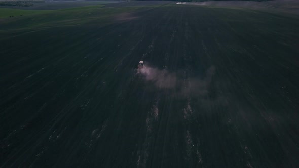 Aerial view of a farmer on a green tractor plowing the dusty arid soil. Agribusiness in the spring