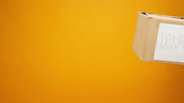 Human Hands Holding Cardboard Box with Coronavirus Donations Against Yellow Background