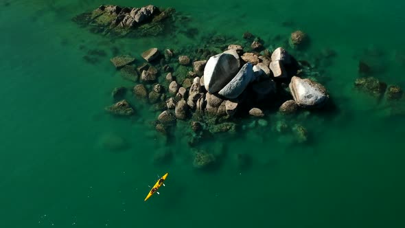 Slowly aerial pan shot of two people canoeing in front of the split apple rock in Abel Tasman Nation