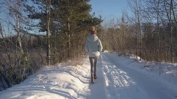 Aerial Backside Girl Walks Along Road in Winter Forest