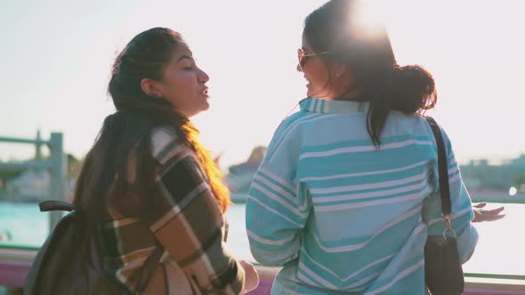 Behind the two female tourists stood talking at the pier. while waiting for the boat ride 