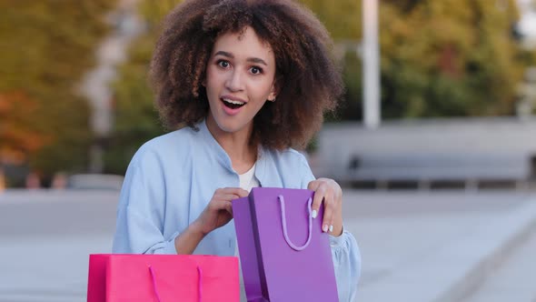 Afro American Woman Young African Girl Sitting on Street Outdoors Holding Gift Bags Looks in Package