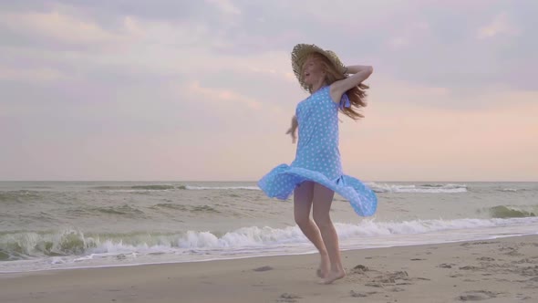 Carefree Woman Dancing on the Sunset on the Sea Beach. Girl Rotate in the Straw Hat . Femininity at