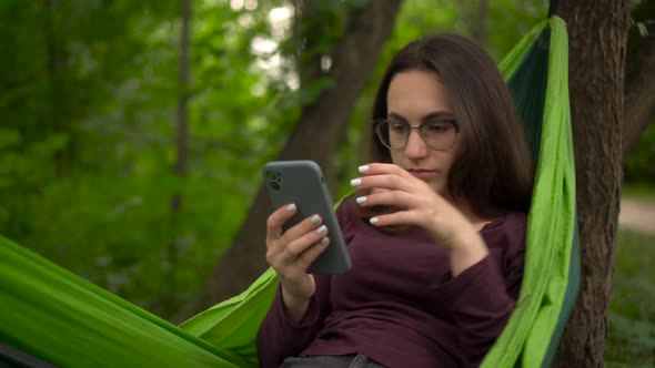 A Young Woman Lies in a Hammock and Chats on the Phone