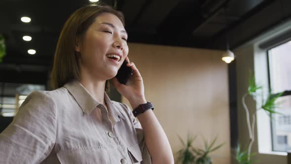 Asian businesswoman standing talking on a smartphone in a modern office