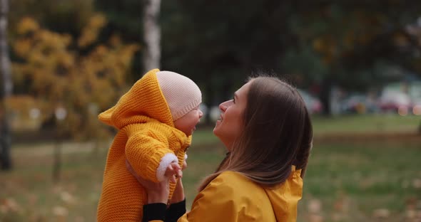 Happy Mother Throws and Catch Her Little Baby at the Autumn Park