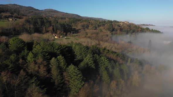 Aerial shot of houses and fog in the forest in Umbria, Italy