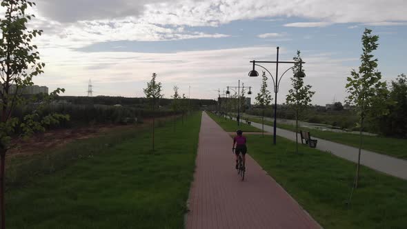 Professional female cyclist in cycling apparel and black helmet is riding on road bike along river