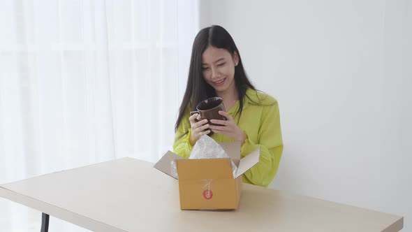Young asian woman unpacking of parcel box with online shopping while satisfied at home.