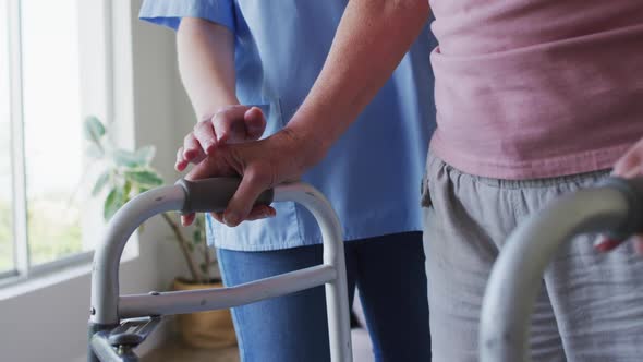 Mid section of female health worker assisting senior woman to walk with walking frame at home