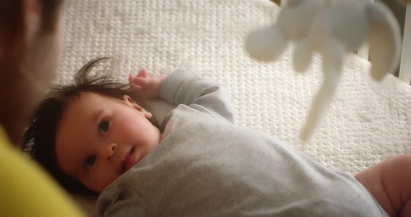 Happy Young Father Strokes Newborn Baby Lying in a Child Crib