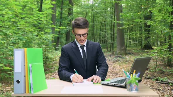 Inspired Businessman Writing His Ideas in Notebook, Sitting at Desk in Forest