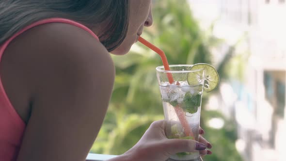 Young Lady in Pink Blouse Bends Over and Sips Cool Mojito