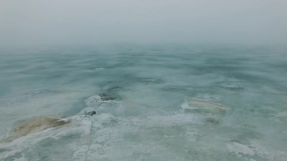 Flight Over Frozen Sea Coast Line With Ice Cracks In Misty Foggy Cold Winter Day