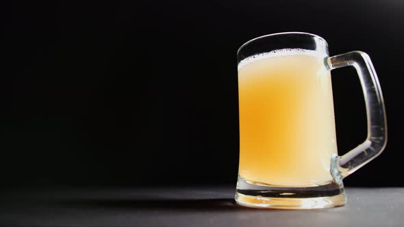 Low Angle Male Hand Putting Big Mug of Fresh Craft Beer on Table Isolated at Black Studio Background