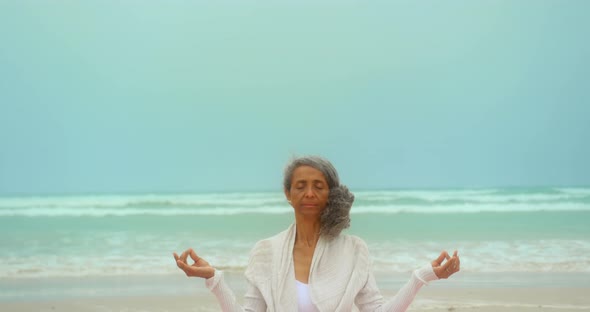 Front view of active senior African American woman doing yoga on exercise mat at the beach 4k