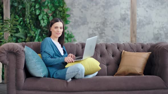 Casual Smiling Businesswoman Sitting with Crossed Legs on Couch at Home Enjoying Weekend