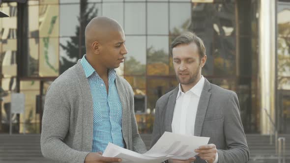 Two Businessmen Examining Documents in Front of Business Building