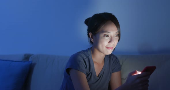 Woman use of mobile phone at night and sit on sofa at home