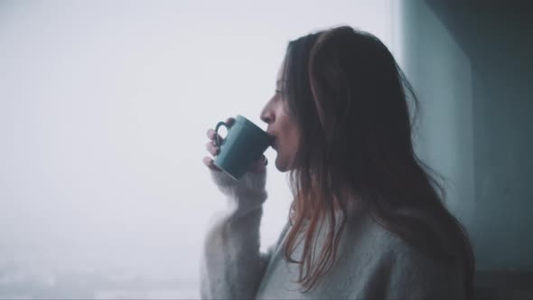 Young woman drinking coffe and watching outside her terrace