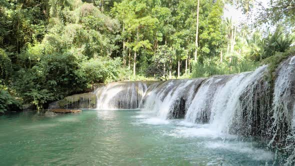 Tripod shot of water flowing from Cambugahay Falls into natural turquoise pool with bamboo raft in S