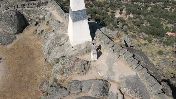 Woman greets drone from megalithic fortification of Monsanto Castle, Portugal. Aerial tilt up reveal