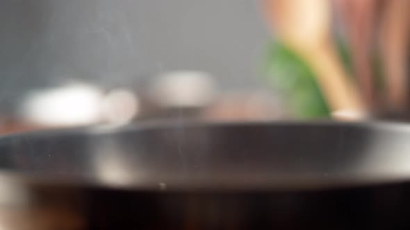 Camera follows adding chopped garlic on cooked bacon in a pan. Slow Motion.