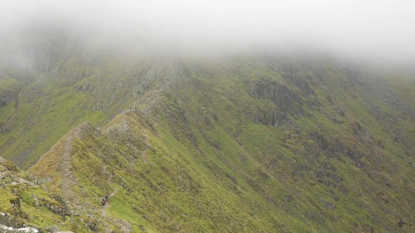 People hiking on mountain trail in a cloudy day