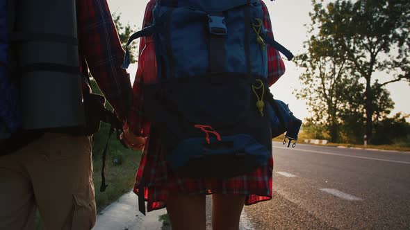 Couple of Tourists with Backpack Walking Along Road Towards Sunset