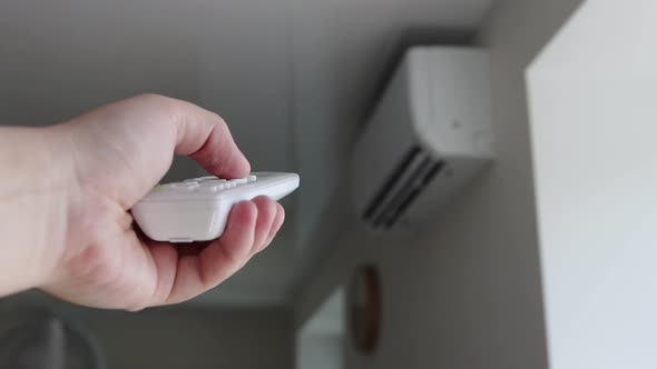 The Man's Hand Holds the Remote Control From the Air Conditioner in His Hand and Controls the