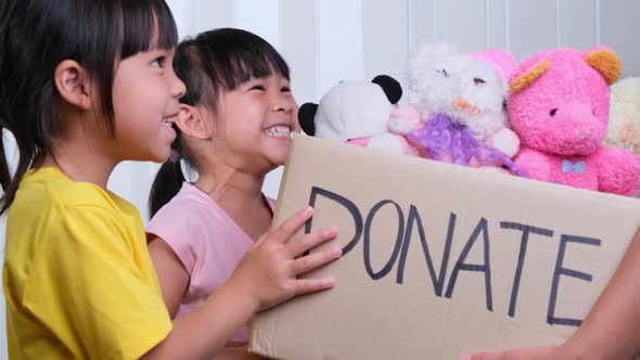 Young woman volunteer giving a donation box with lots of dolls to the children.