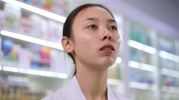 Headshot Portrait of Intelligent Asian Young Beautiful Woman Choosing Pills on Shelves in Pharmacy