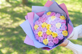A bouquet of lilac and yellow candy roses is in paper in hands on a green background. - PhotoDune Item for Sale