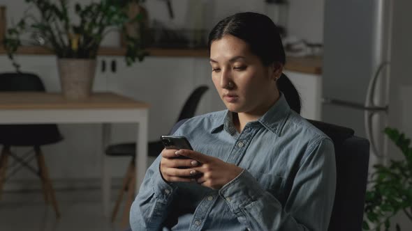 Close up portrait of cheerful asian woman texting on cellphone, chatting with friends at home