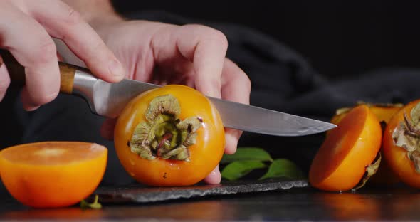 Male Hand with a Knife Cut the Persimmon in Half