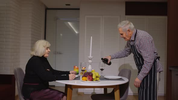 Senior Retired Couple Having Fun Drinking Wine and Eating Meal During Romantic Supper in Kitchen