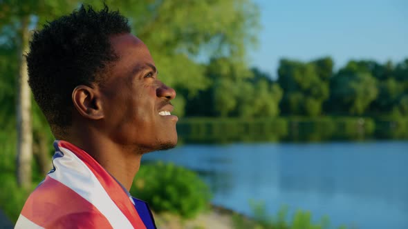 Smiling AfroAmerican Man with American Flag on Shoulders Looks at Sunrise