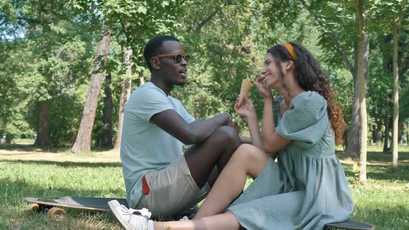 Different Races Couple Sits on Grass Eating Icecream Cones