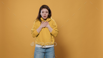 getting scared and anxious in studio. Panicked casual young adult wearing hoodie choking because of shock and anxiety over yellow background.
