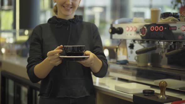 Unrecognizable Caucasian Bartender Holding Cup with Tea or Coffee and Smiling. Young Positive Woman