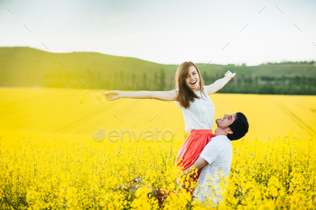 g on man`s hands, pose together on yellow flower field during sunny summer weather. Romantic couple have fun outdoor. Relationships concept.