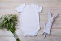 White baby short sleeve bodysuit mockup with wild flowers and bunny rabbit toy - PhotoDune Item for Sale