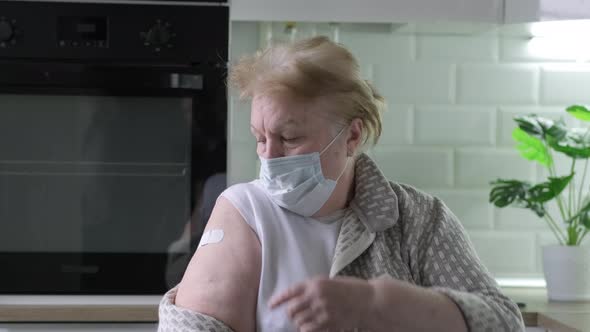 Senior Woman in Face Mask Showing Bandage on Arm After Covid Vaccination